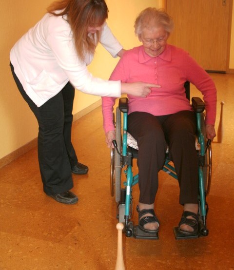 Therapeutin begleitet eine Seniorin im Rollstuhl